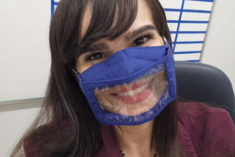 Descrição da imagem Foto de Raphaela Giffoni (Presidente da Comissão UFF Acessível), mulher branca de cabelo castanho comprido.  Ela sorri e usa uma máscara azul com o visor transparente na altura dos lábios, veste uma blusa com estampa de onça e uma jaqueta em tom de vinho.