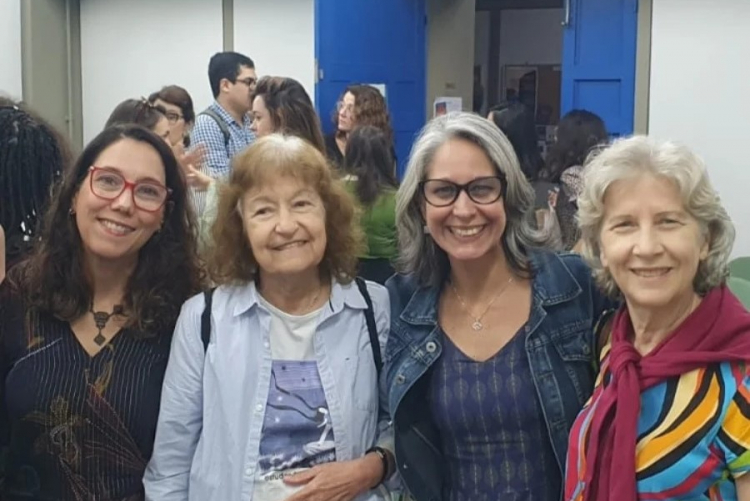 #ParaTodosVerem As professoras Letícia de Oliveira, de cabelo castanho e óculos com aro vermelho, Hildete Pereira, com cabelos ruivos, Karin Calaza, de cabelos grisalhos e óculos com aro preto, e Eliane Volchan, também de cabelos grisalhos, sorriem na foto durante um evento do livro “Mulheres na Ciência: O que mudou e o que ainda precisamos mudar”