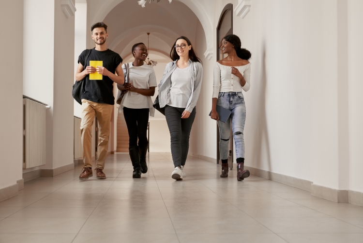 grupo de quatro estudantes multirraciais caminhando pelo corredor de uma faculdade
