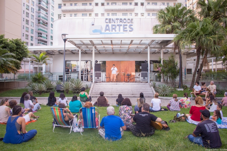 várias pessoas sentadas de costas nos jardins da reitoria da UFF, assistindo a uma apresentação musical