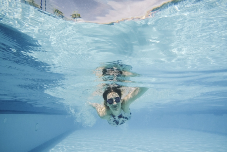 Imagem: mulher com óculos de mergulho nadando em uma piscina azul