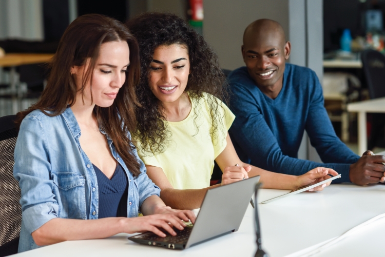 imagem: uma mulher digitando no notebook e duas pessoas ao lado olhando