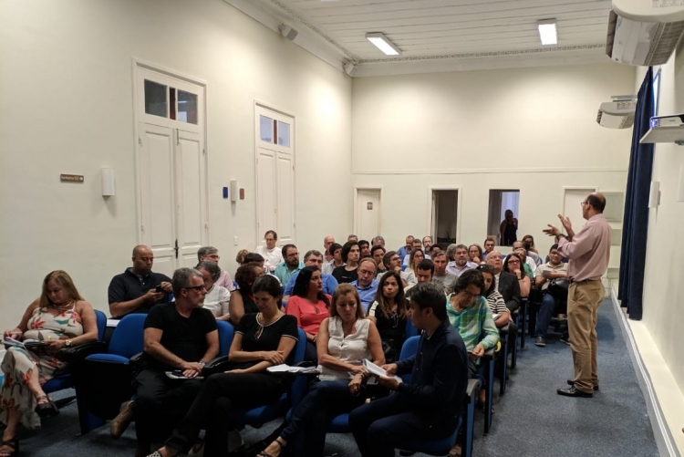 Foto de uma sala de reunião, em que aparece o Prof. Fábio Passos palestrando para um grupo de gestores da UFF.