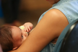 #ParaTodosVerem A imagem mostra um bebê de pele clara, cabelo castanho e roupa amarela deitado nos braços de uma mulher que veste uma camisa azul clara sem mangas