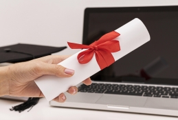 Mão de mulher segurando diploma na frente de um notebook