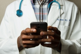 Médico com estetoscópio em volta do pescoço segura com as duas mãos um celular