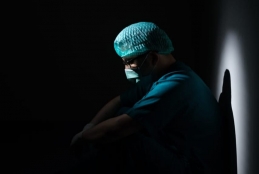 Um profissional da saúde vestido com EPIs sentado no chão, em um lugar escuro