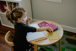 criança com máscara brincando sentada em uma mesa
