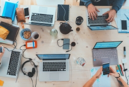 Uma mesa repleta de laptops abertos sendo manuseados
