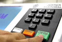 Pessoa tocando no botão confirma da urna eletrônica durante processo eleitoral