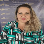 Mulher branca, cabelo loiro, blusa colorida em tons de verde, branco e preto.
