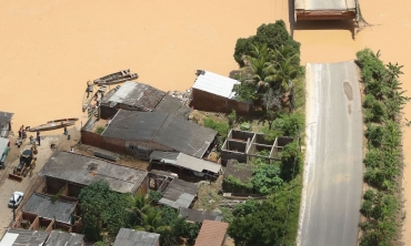 Imagem aérea que contém telhados, uma rodovia partida ao meio e água barrenta chegando aos telhados das casas