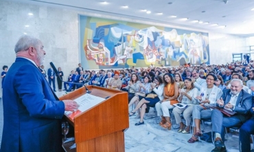 Foto do encontro de reitores e diretores das Instituições Públicas de ensino superior. Na imagem, o presidente Lula está com um terno de cor azul, em pé em um púlpito realizando o discurso. Na sua frente, a plateia está sentada e é composta por representantes de Universidades e Institutos Federais