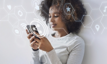 Mulher negra com celular na mão acessando à internet. Ícones simbolizando o acesso em redes encontram-se no layout na cor branca.