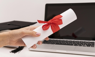 Mão de mulher segurando diploma na frente de um notebook