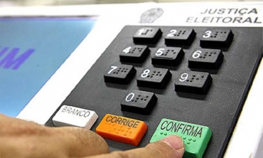 Pessoa tocando no botão confirma da urna eletrônica durante processo eleitoral