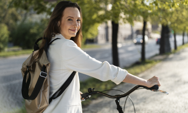 Mulher de cor branca e cabelo preto, com mochila nas costas e blusa branca, segurando sua bicicleta